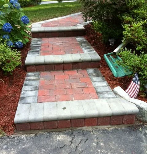 Brick and stone tiered garden pathway with blue hydrangeas and red mulch landscaping