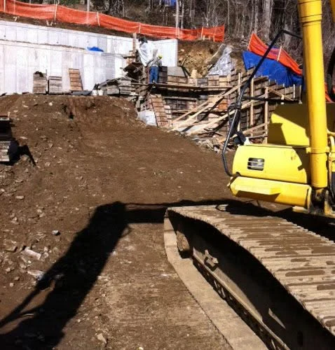 Construction site with yellow excavator, dirt lot, wooden deck, and safety barriers