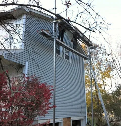 Light blue two-story house with bare branches and autumn foliage visible