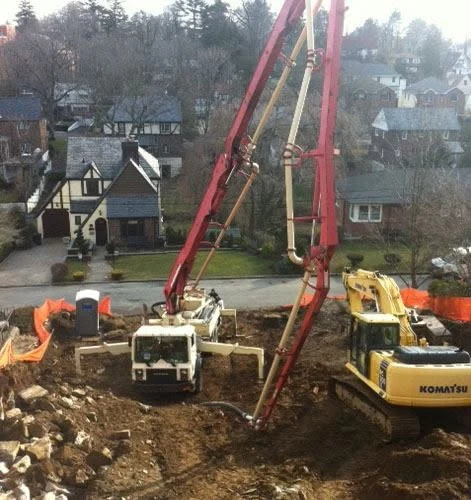 Concrete pump truck pouring foundation at residential construction site with excavator and workers