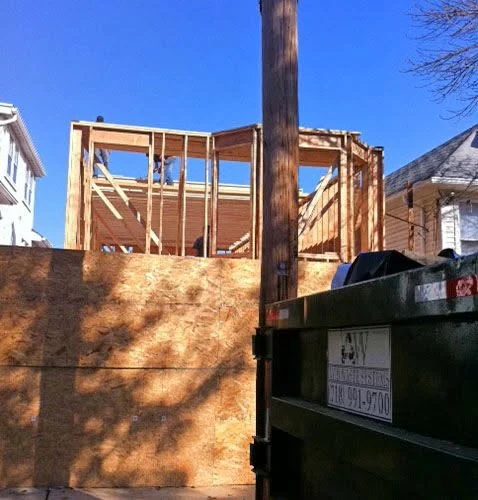 Construction framing of wooden house structure with brick foundation and utility dumpster