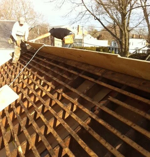 Workers installing roof shingles on residential house during renovation