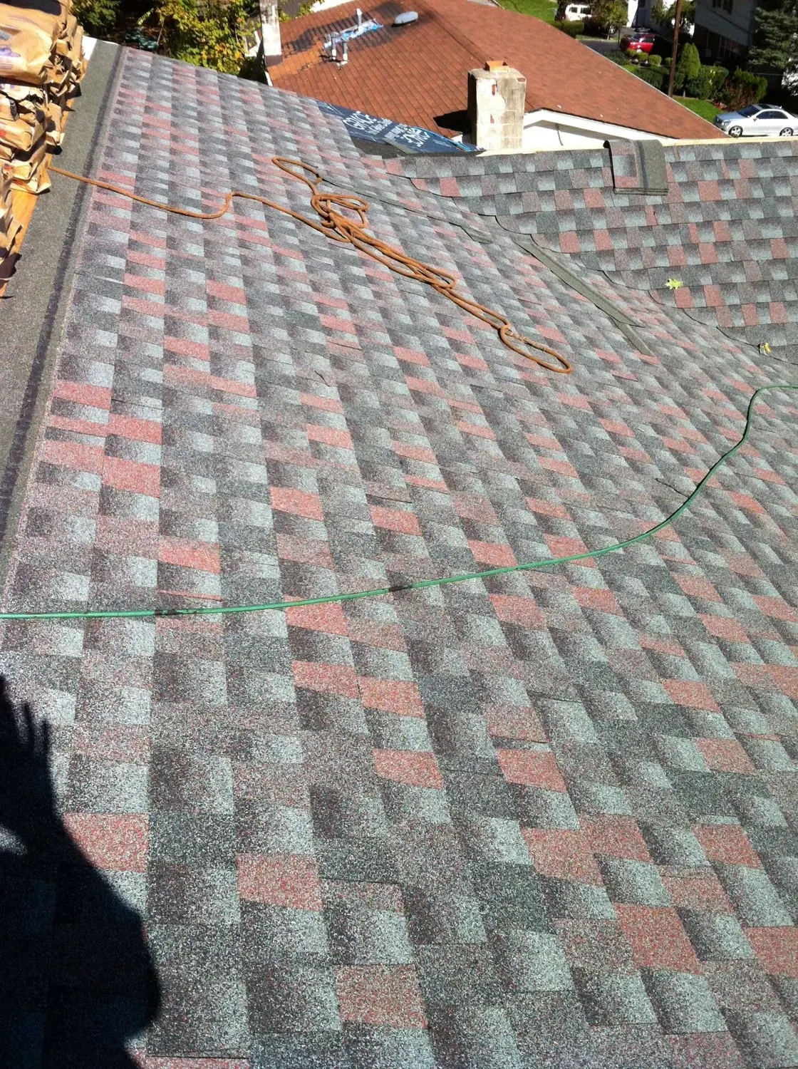 Aerial view of asphalt shingle roof with gray and red diamond pattern during installation with copper flashing and green cable visible